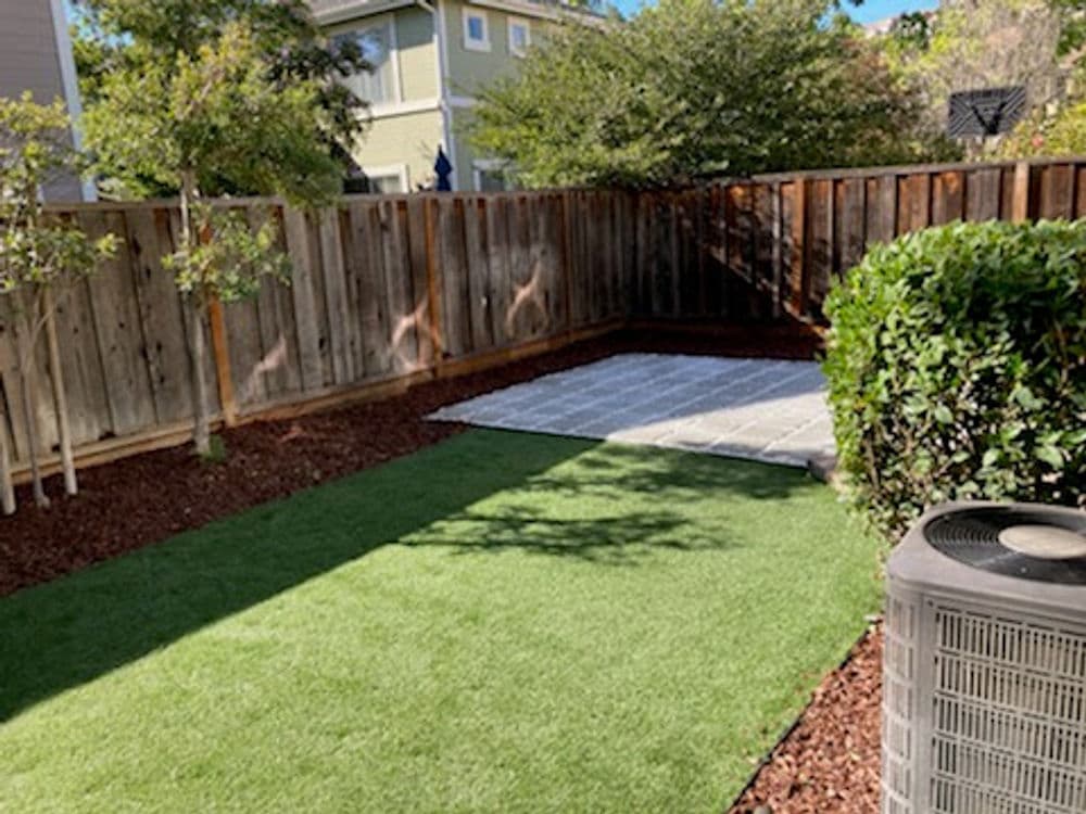 Backyard landscape with artificial turf, gravel area, and wooden fence for outdoor relaxation.