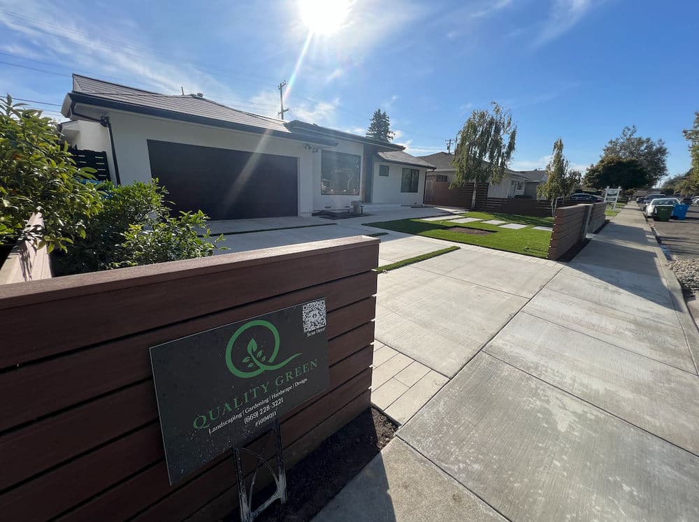 Modern house exterior with landscaped yard, green plants, and a sign for Quality Green.